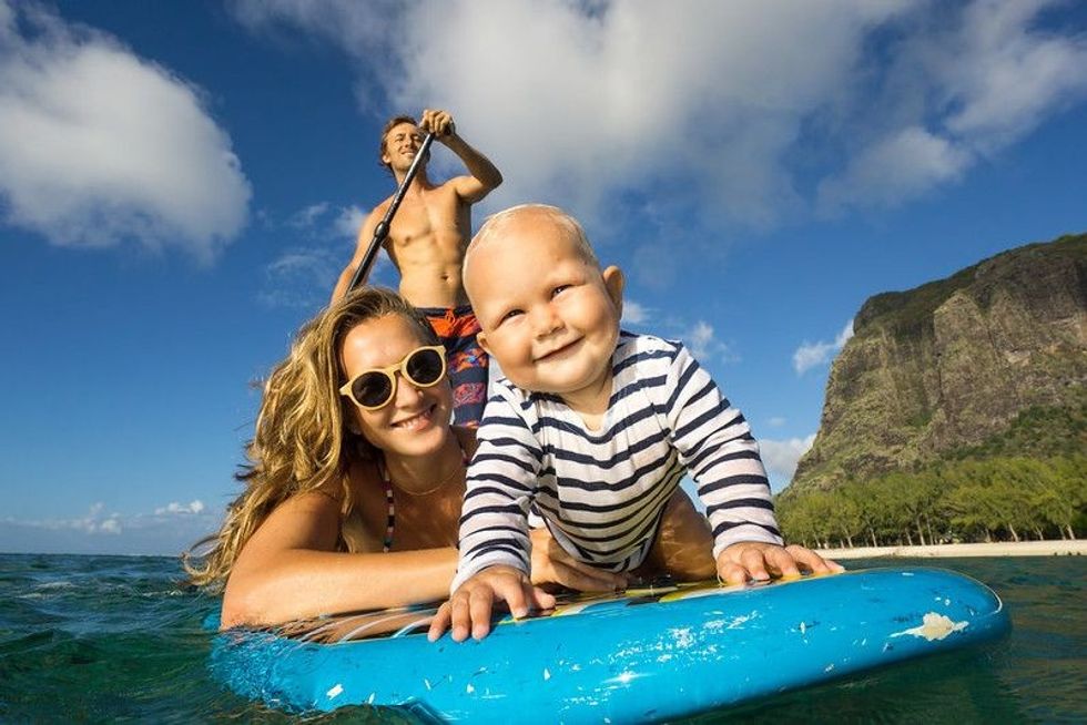Young and beautiful parents ride by surfboard with baby