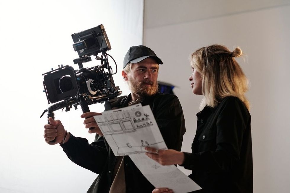 Young bearded cameraman and his assistant with documents consulting about shooting