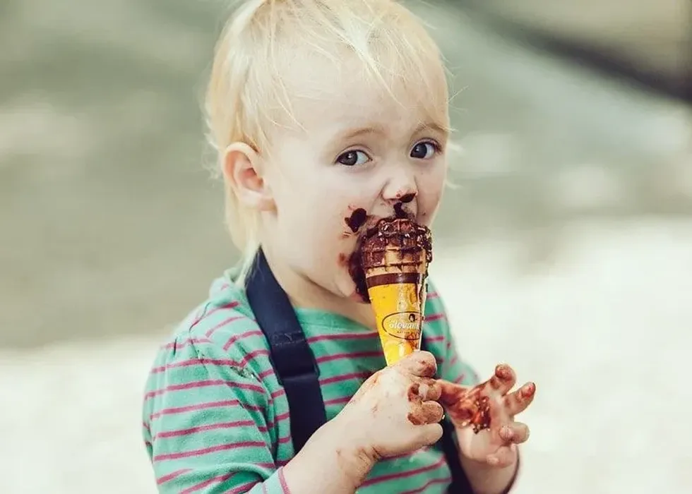 Young boy eating a cone of chocolate ice cream has chocolate all over his face.