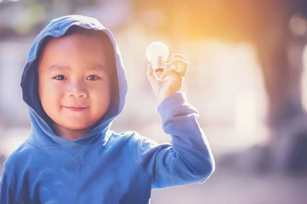 Young boy wearing a blue hooded jumper holding up a lightbulb.