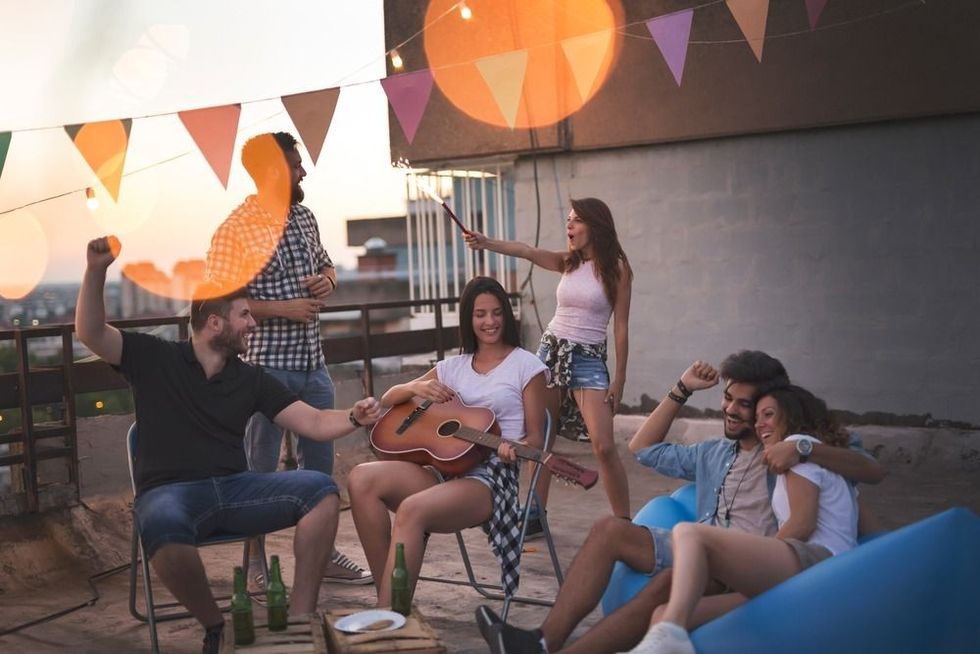 Young friends having fun at a rooftop party, playing the guitar, singing, dancing and chilling out.