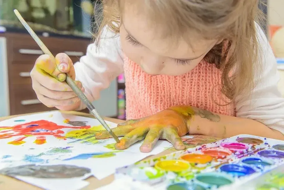 Young girl enjoying messy play and painting on her hand.