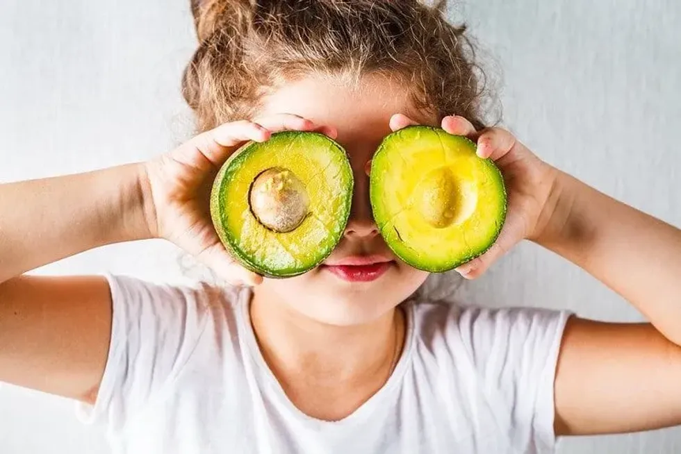 Young girl messing around holding avocado halves in front of her eyes.
