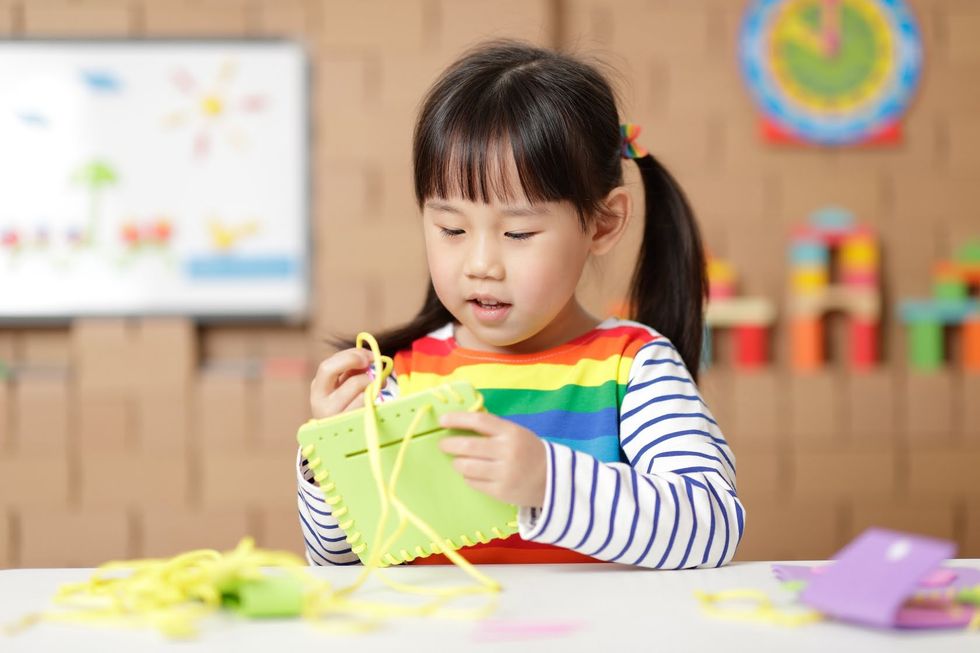 Young girl sewing a pad using plastic needle and yellow yarn at home
