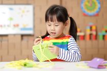 Young girl sewing a pad using plastic needle and yellow yarn at home