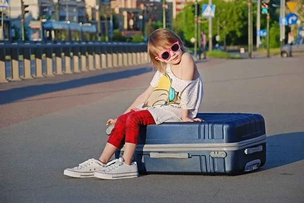 Young girl sitting on a suitcase wearing sunglasses and posing on holiday.