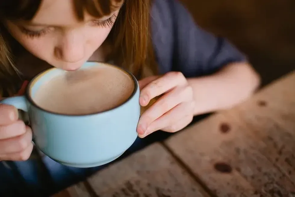 Young girl taking a sip from a huge blue mug of coffee.