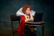 Young girl with curly red hair dressed in old fashioned royal person working on a laptop