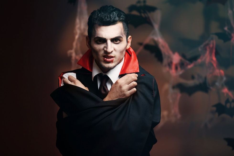 Young man dressed as vampire for Halloween party, on dark background