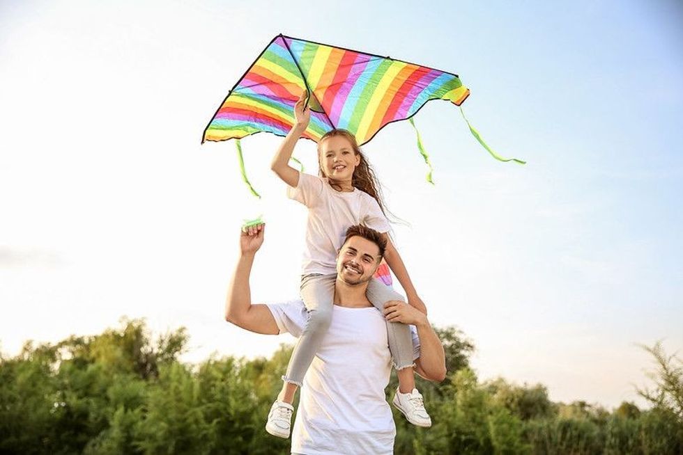Young man with little daughter flying kite outdoors