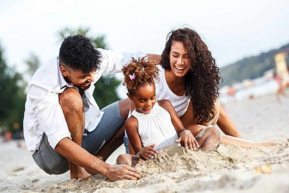 Young mixed race family sitting and relaxing at the beach on beautiful summer day.