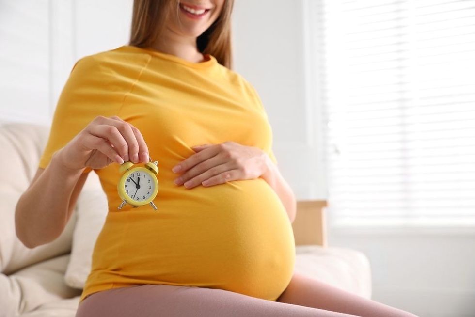 Young pregnant woman holding alarm clock