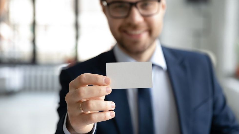 Young smiling businessman showing blank mock up company card to camera