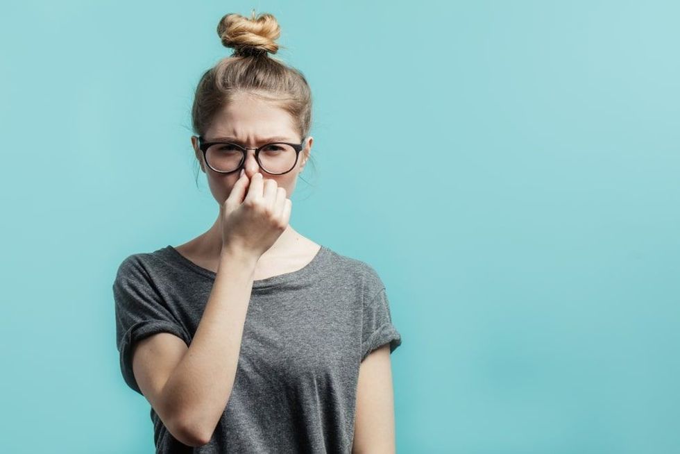 Young student girl with hair bun in casual t-shirt squeezing nose with fingers
