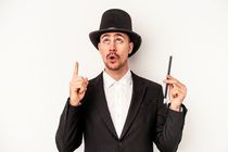Young wizard holding a wand isolated on white background pointing upside with opened mouth.