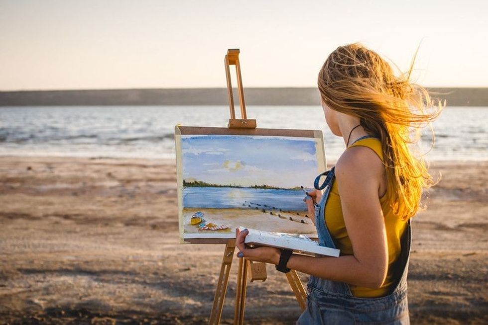 Young woman artist painting landscape in the open air on the beach.