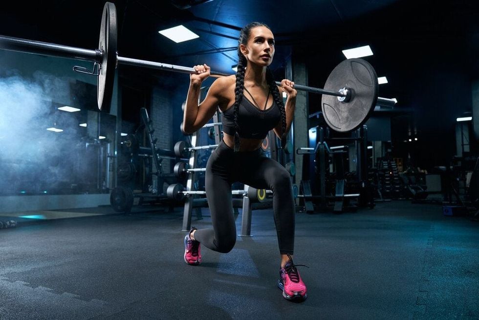 Young woman exercises in gym holding barbell on shoulders.