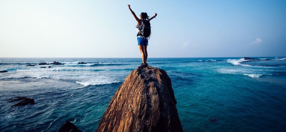 Young woman hiker with outstretched arms on seaside rock cliff edge