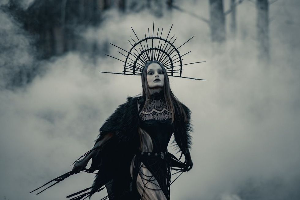 Young woman in black dress and crown on her head in dark and foggy forest