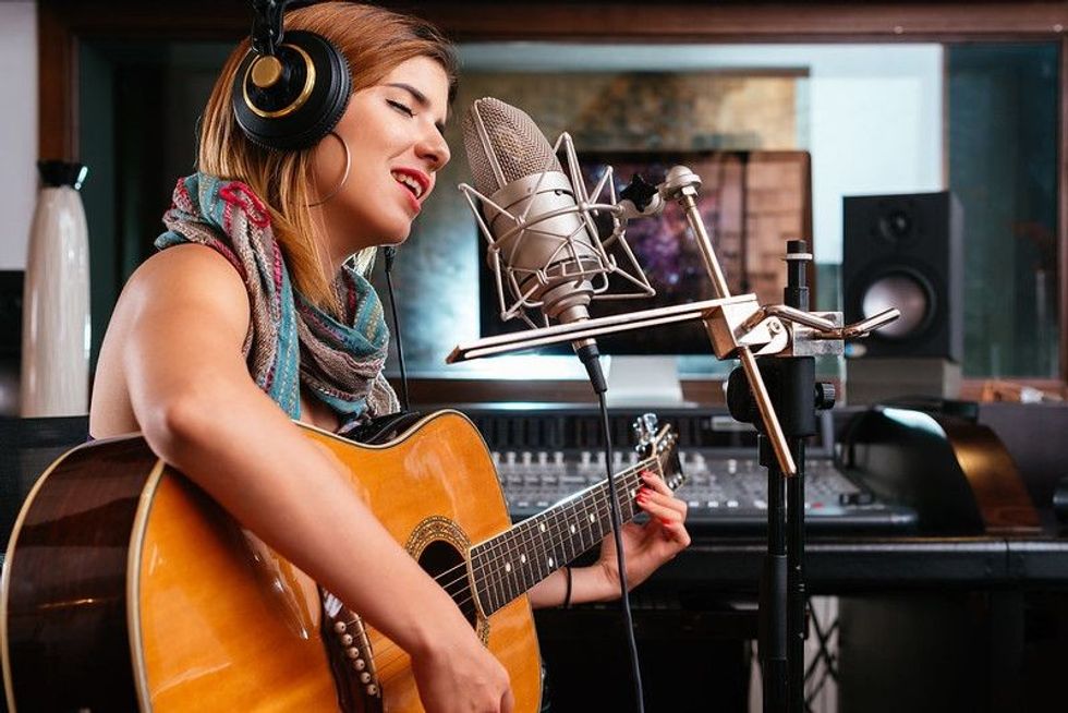 Young woman with guitar recording a song in the studio.