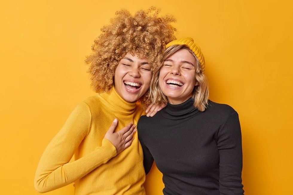 Young women laughing together dressed casually isolated over yellow wall.