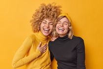 Young women laughing together dressed casually isolated over yellow wall.